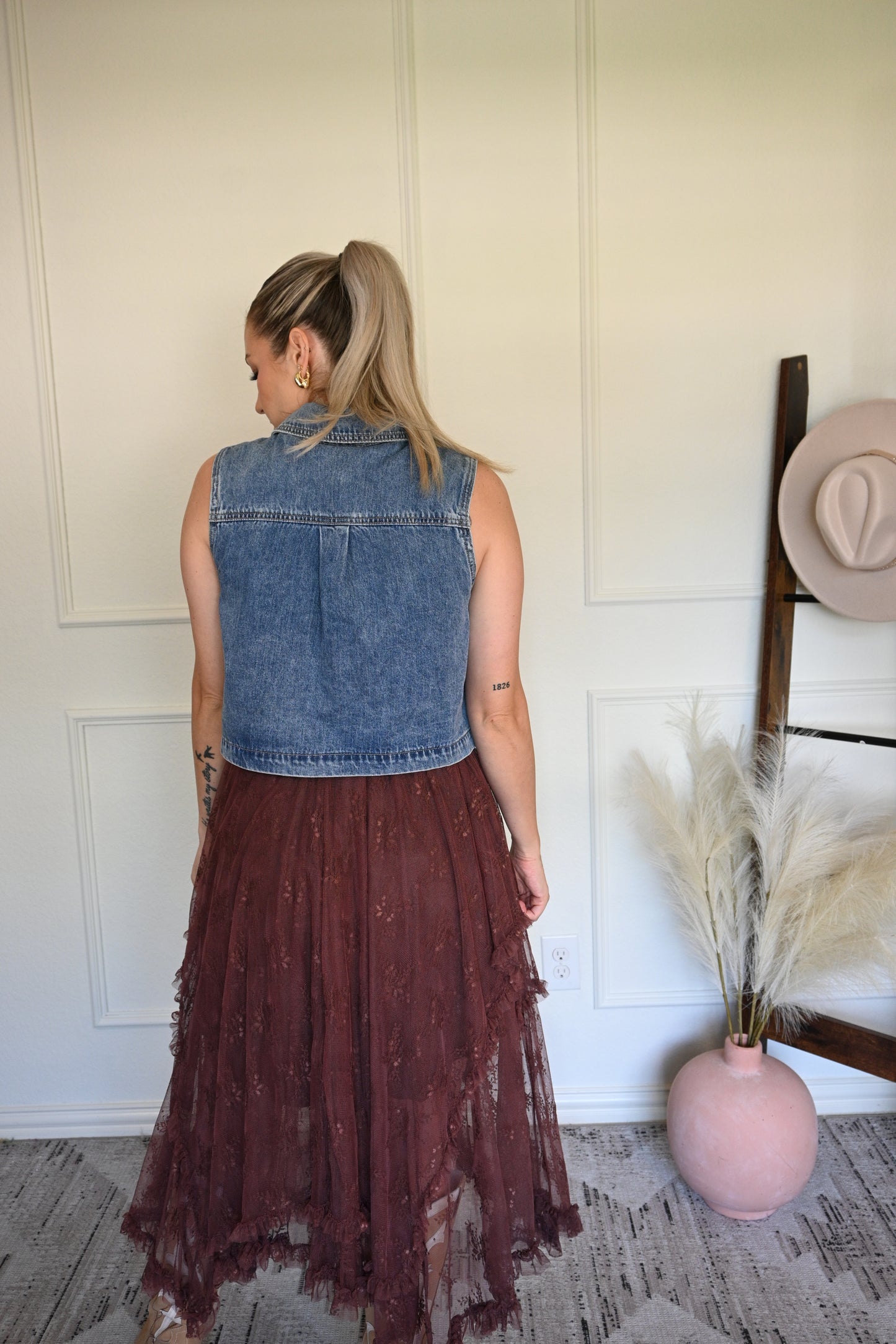 Woman holding a long brown lace skirt and a denim vest top