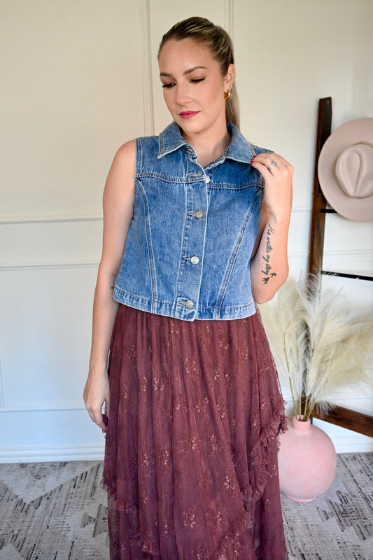 Woman wearing a denim vest and a brown skirt, standing indoors.