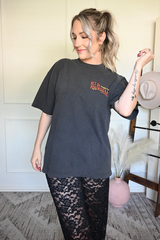 Woman wearing a washed black t-shirt with text, standing in a room with a white wall and decorative items