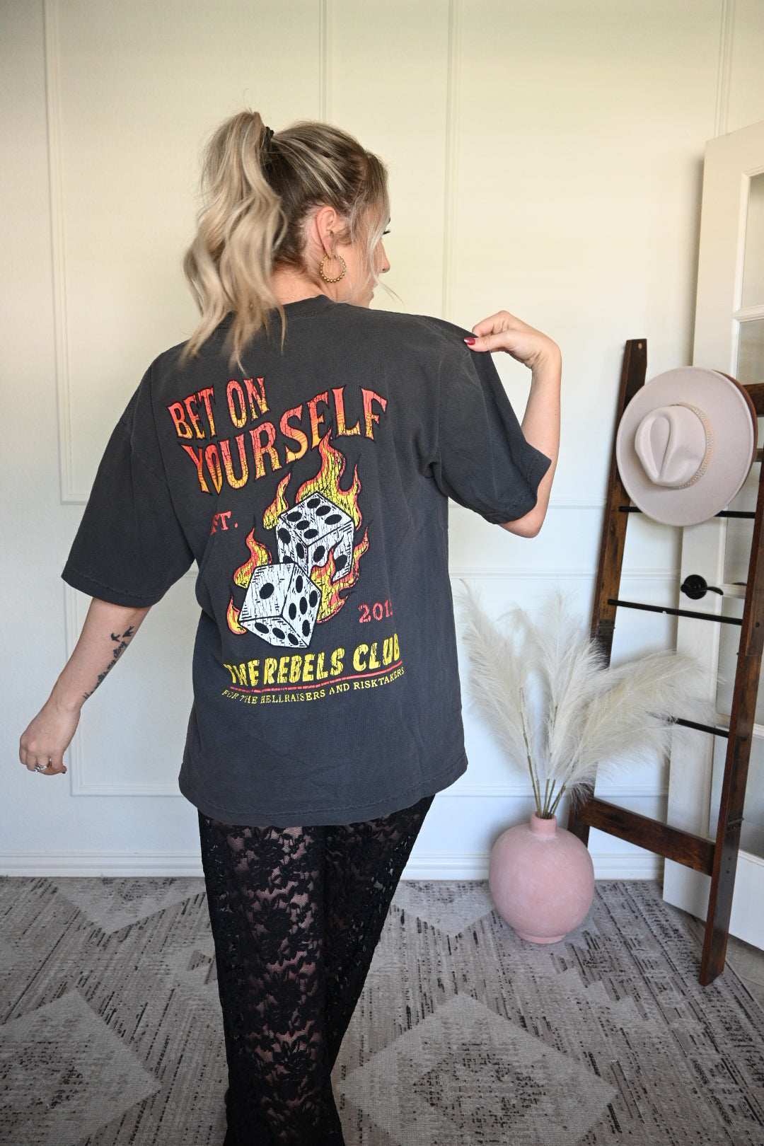 Person wearing a black t-shirt with graphic design and text, standing indoors.