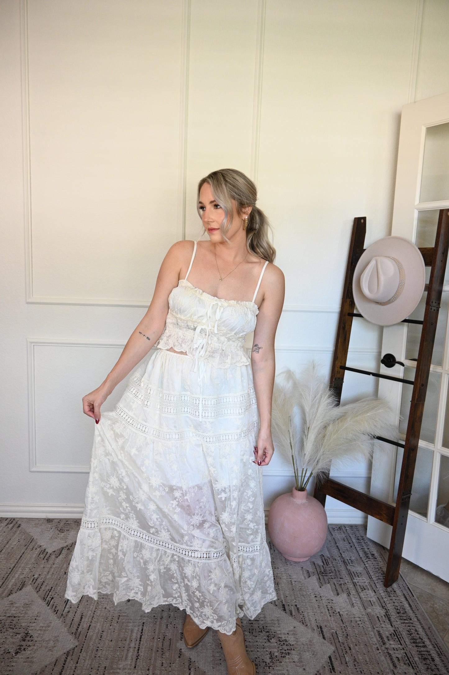 Woman holding one side of the top and lace skirt set in a room with a wooden floor and white walls.