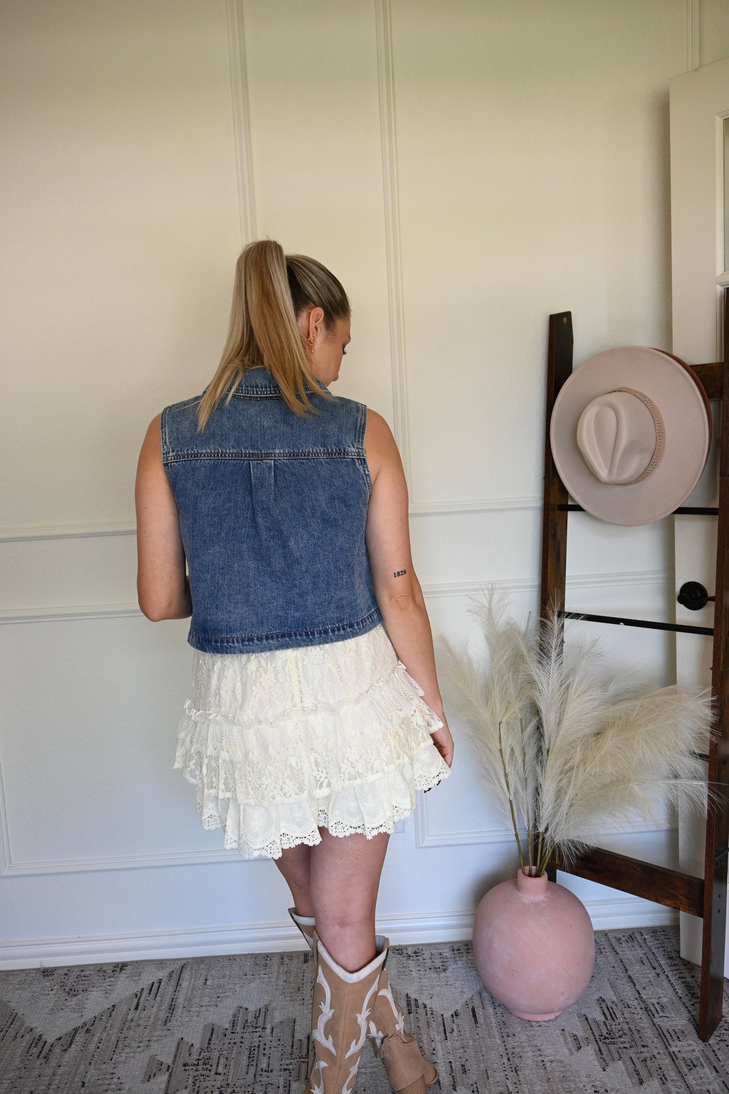 Woman in denim vest in a room with a hat rack and decorative items.