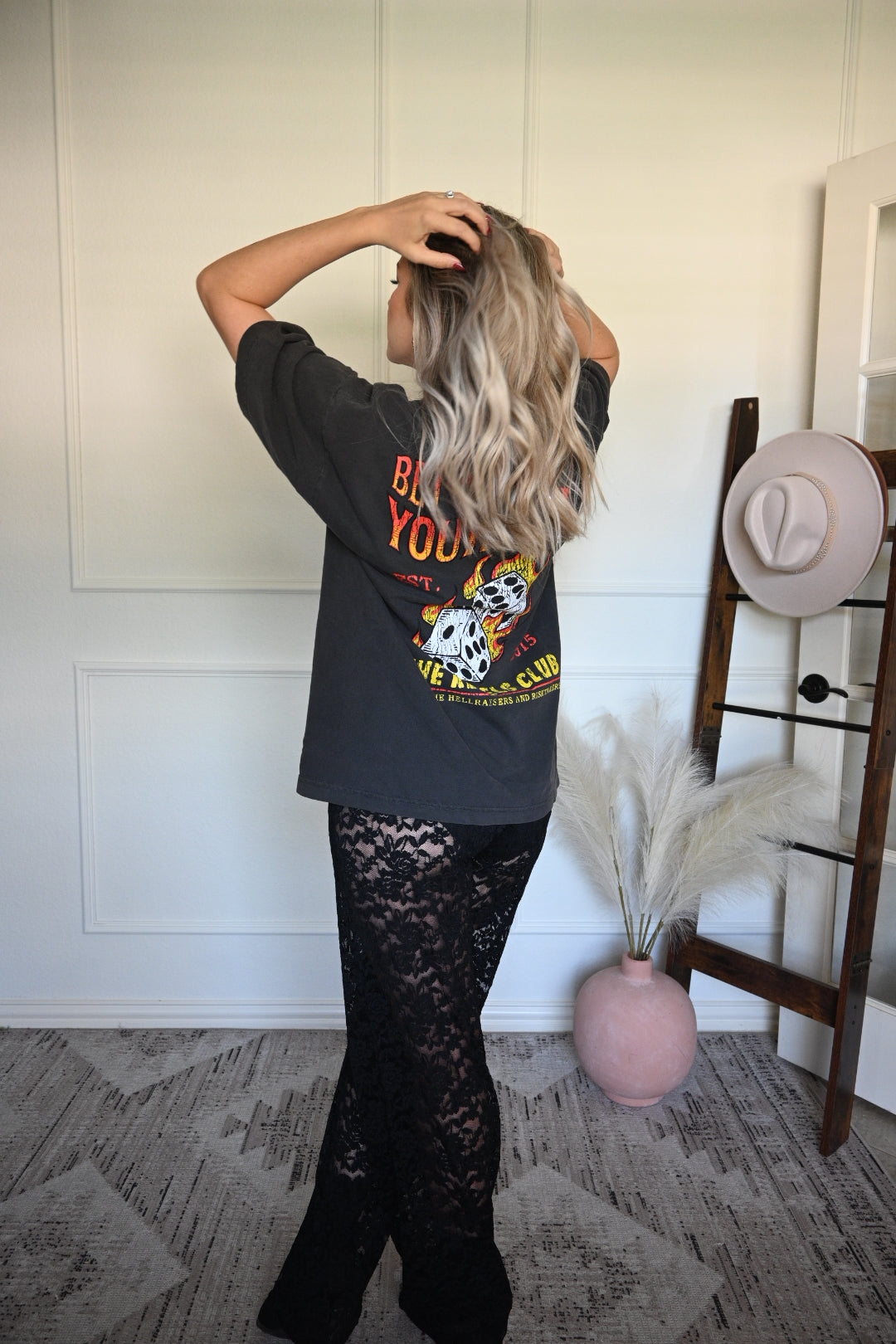Person wearing a black graphic tee with a graphic design, standing in a room with a white wall and wooden floor.