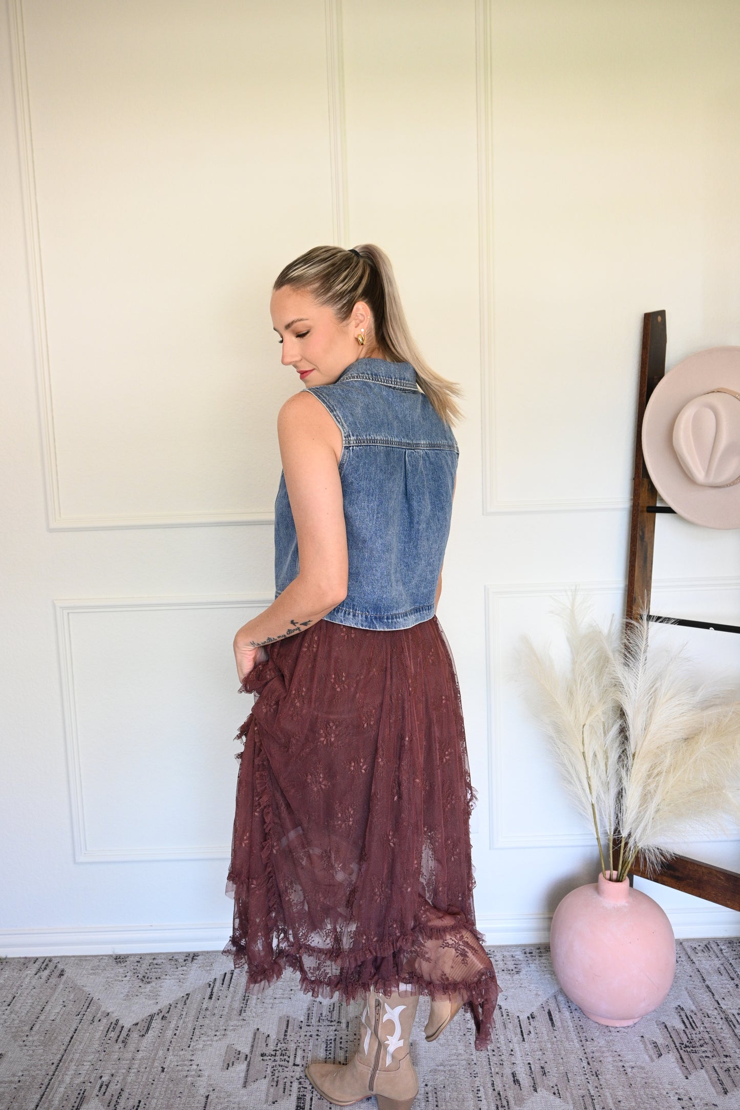 Woman holding a brown lace skirt in a room with a white wall and wooden floor.