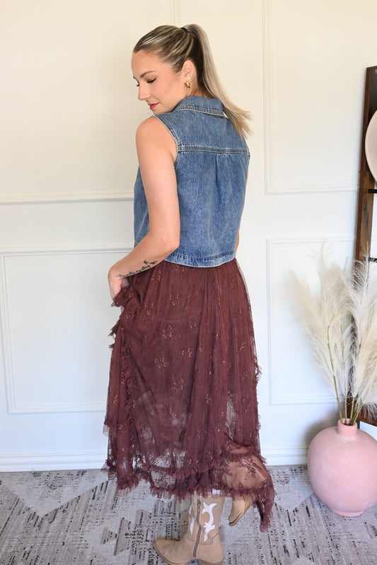 Woman holding a brown lace skirt in a room with a white wall and wooden floor.