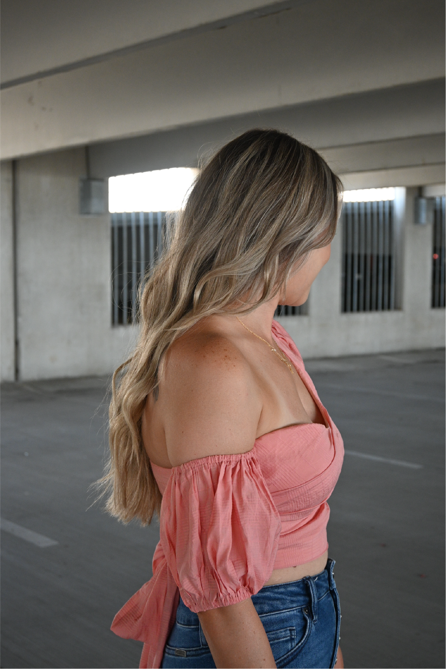 Model is showing the coral colored darling cropped top from the right side, off the shoulder paired with the high rise kancan bootcut jeans.
