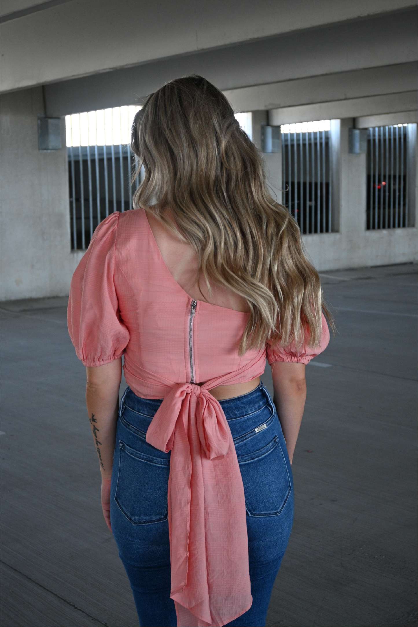 Model is showing the back of the coral colored darling cropped top from the back with zipper down the back and tie in the back.