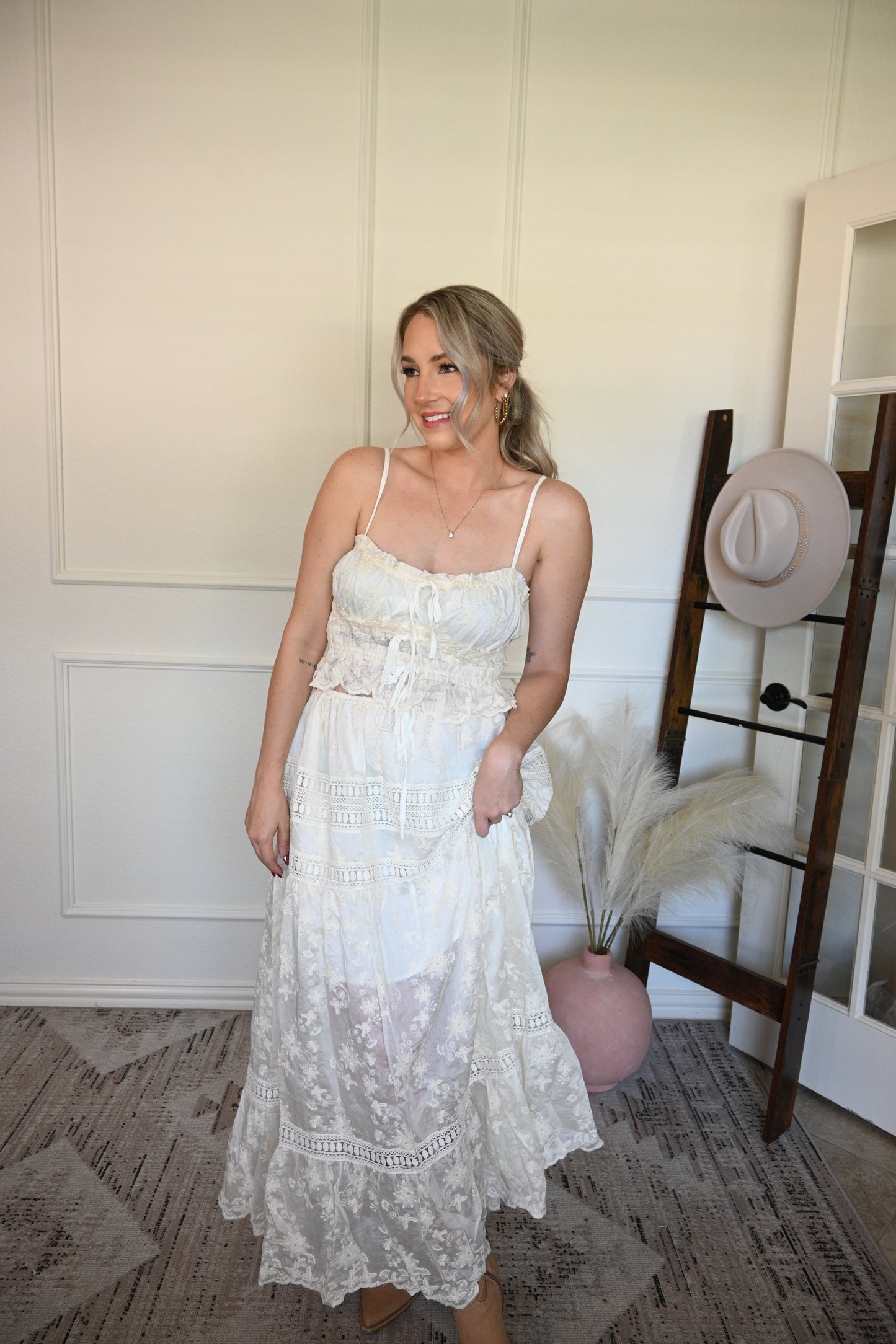 Woman holding a ivory top and lace skirt set in a room with a wooden floor and white walls.
