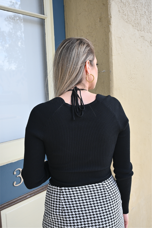 Model is showing the back of the black sweater bodysuit paired with the houndstooth mini skirt.