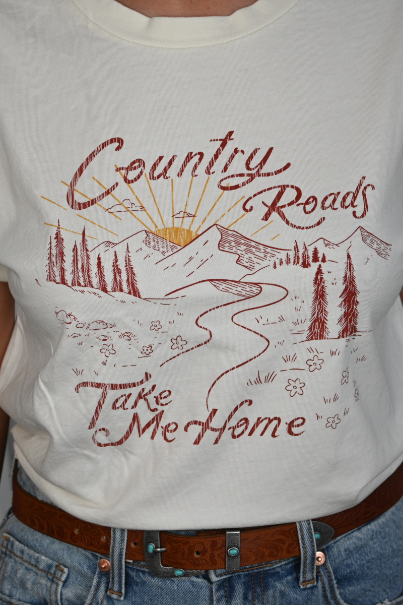 Close up of a vintage white graphic tee with an illustration of mountains and a long road. The shirt says COUNTRY ROADS TAKE ME HOME.