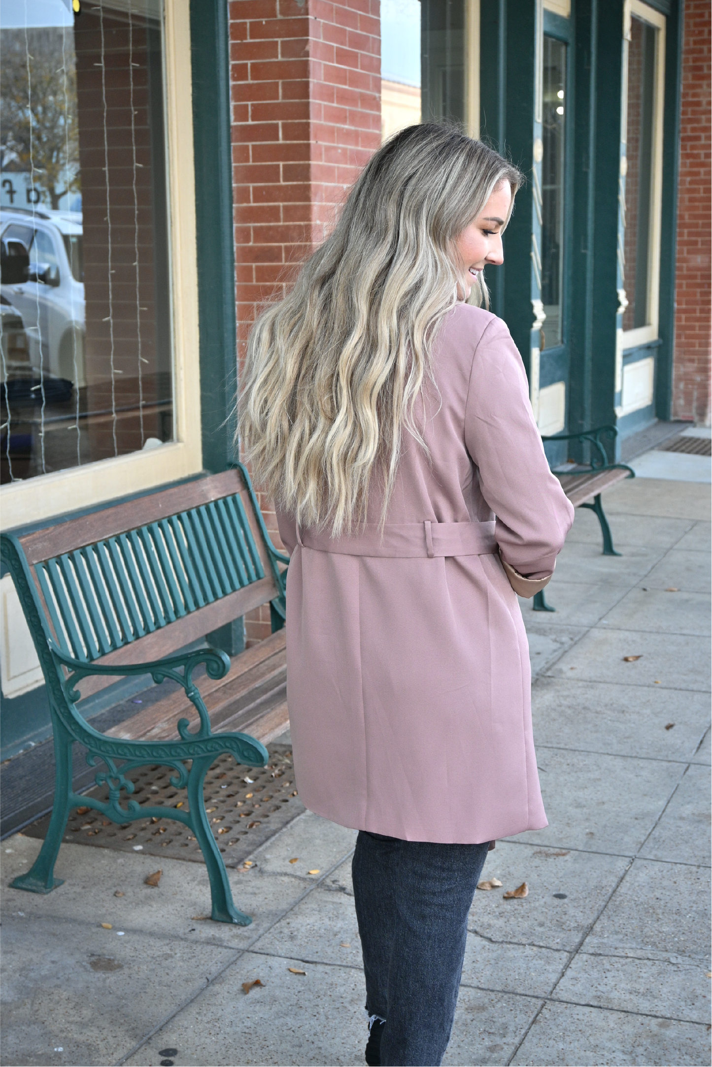 A woman is turned away showing the back of an oversized belted blazer in mocha paired with dark grey distressed skinny jeans.