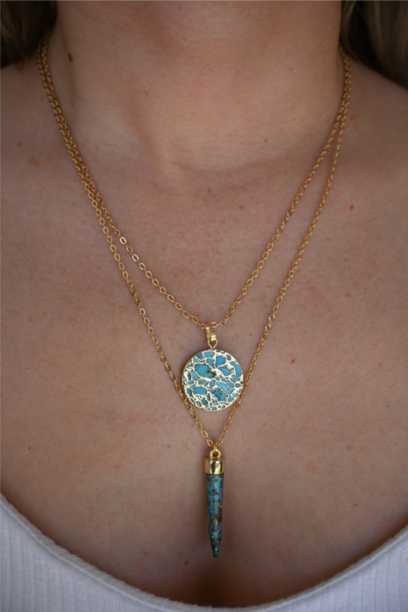 A close up image of a women wearing the circle turquoise stone gold necklace paired with the turquoise spike necklace.