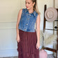 Woman wearing a denim vest with a brown lace skirt in a room with decorative elements.