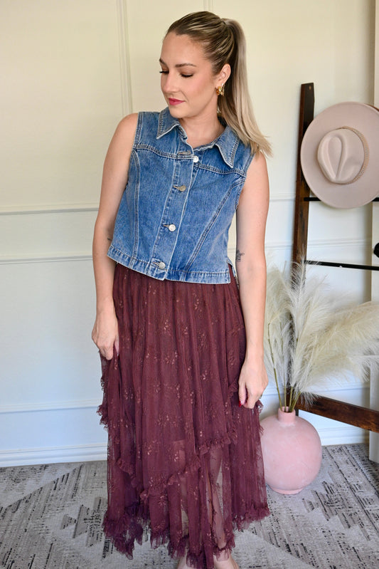 Woman wearing a denim vest with a brown lace skirt in a room with decorative elements.