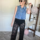 Person wearing black lace pants and denim vest standing on a decorative rug.