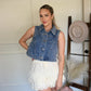Woman in a denim vest standing next to a hat on a stand indoors.