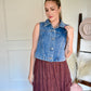 Woman wearing a denim vest and a brown skirt, standing indoors.