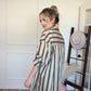 Woman wearing a striped shirt/dress standing in a room with a white wall and decorative rug