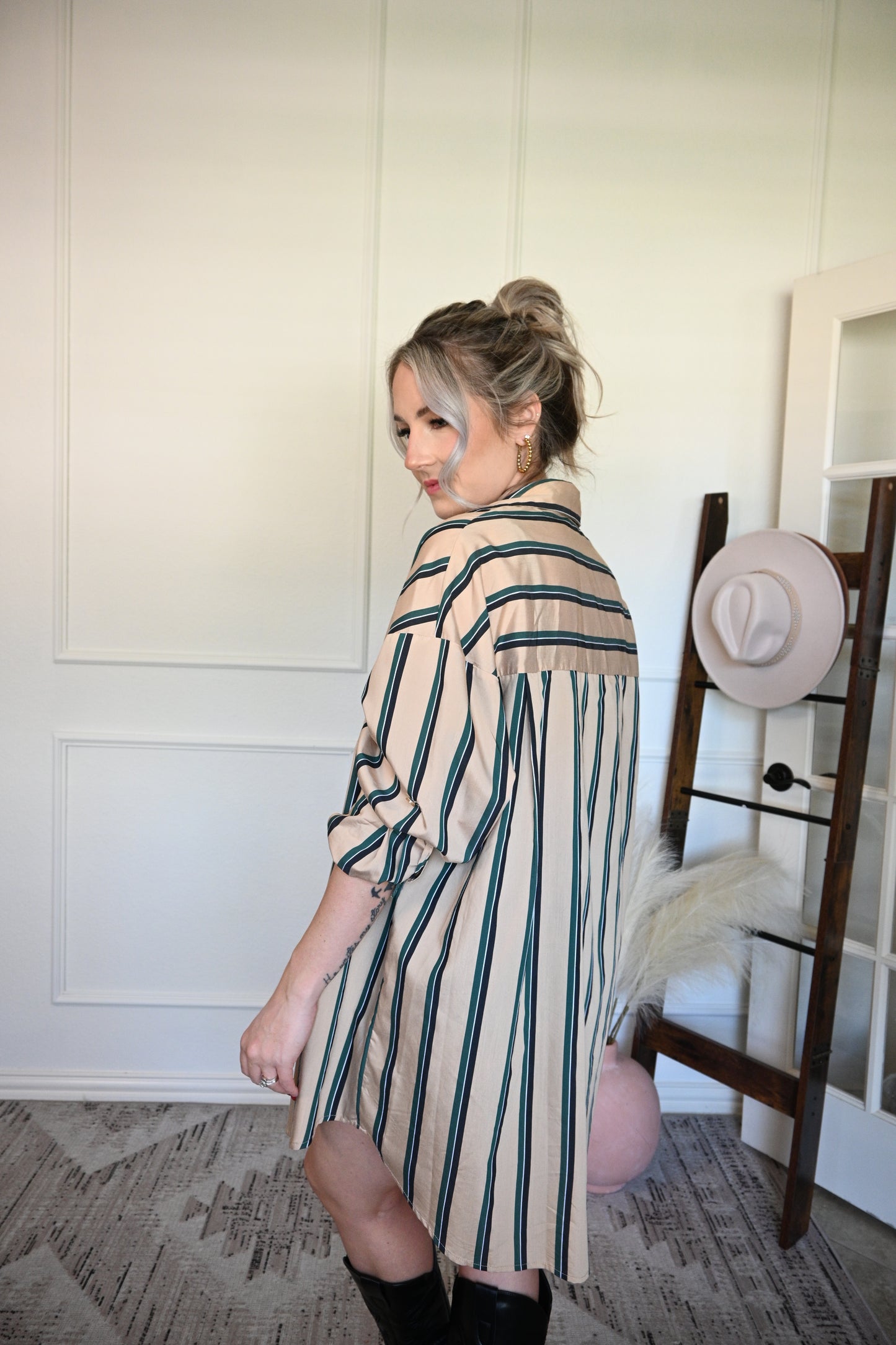 Woman wearing a striped shirt/dress standing in a room with a white wall and decorative rug