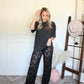 Woman in black lace pants and black oversized graphic tee with a white wall and patterned rug.