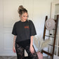 Person wearing a black graphic tee tucked in to black sheer lace pants standing on a decorative rug
