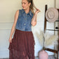 Woman holding her ponytail wearing a denim vest with a brown lace skirt