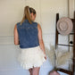 Woman in denim vest in a room with a hat rack and decorative items.