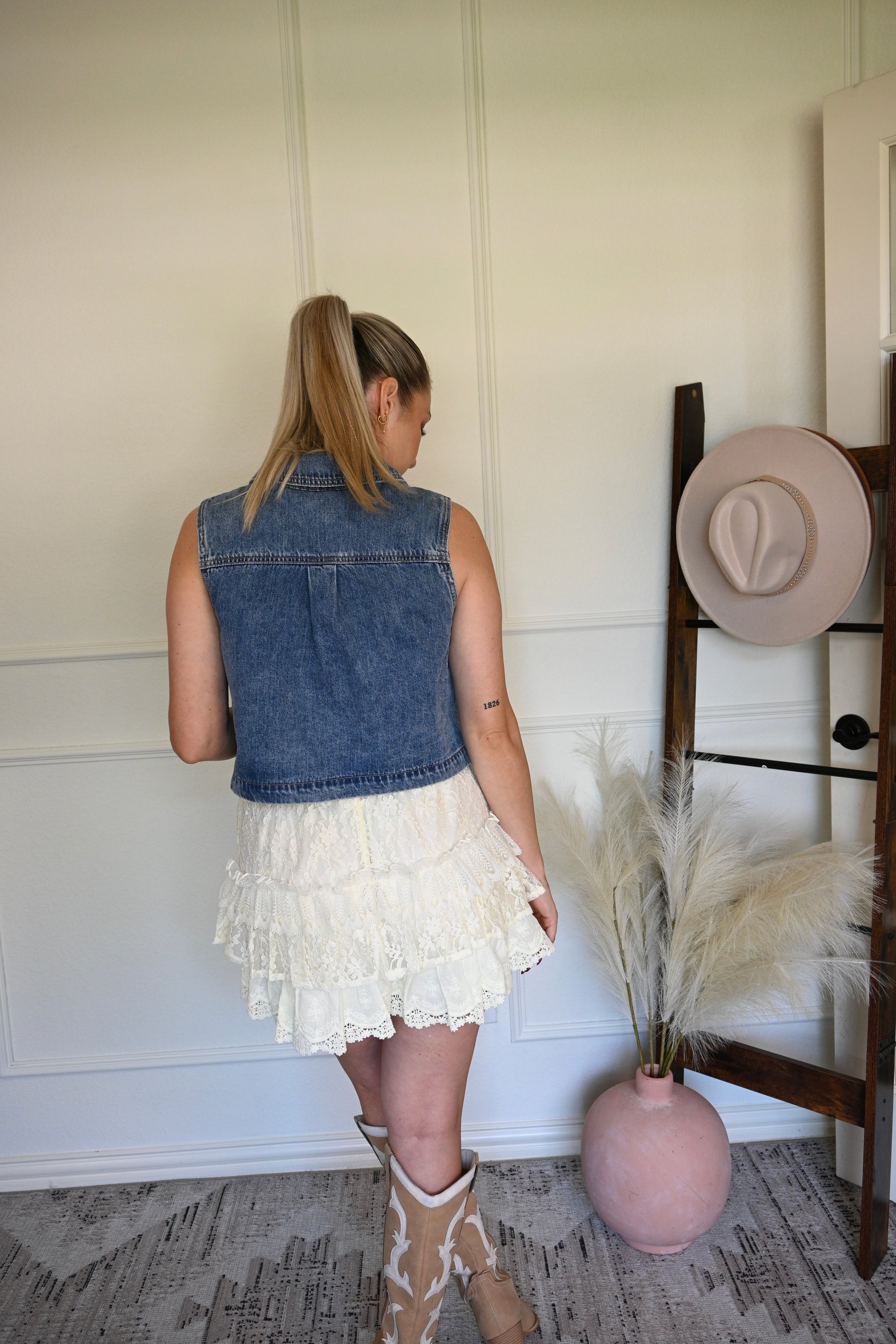 Woman in denim vest in a room with a hat rack and decorative items.