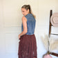 Woman holding a brown lace skirt in a room with a white wall and wooden floor.