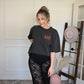 Person wearing an oversized graphic tee with text and lace pants standing in a room with a mirror and hat.