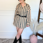 Woman wearing a striped shirt/dress with black boots in a room with a white wall and decorative elements.