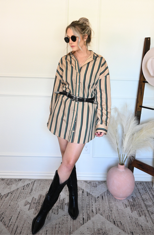 Woman wearing a striped shirt/dress with black boots in a room with a white wall and decorative elements.