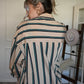 Person wearing a striped shirt/ dress standing in a room with a white wall and wooden floor.