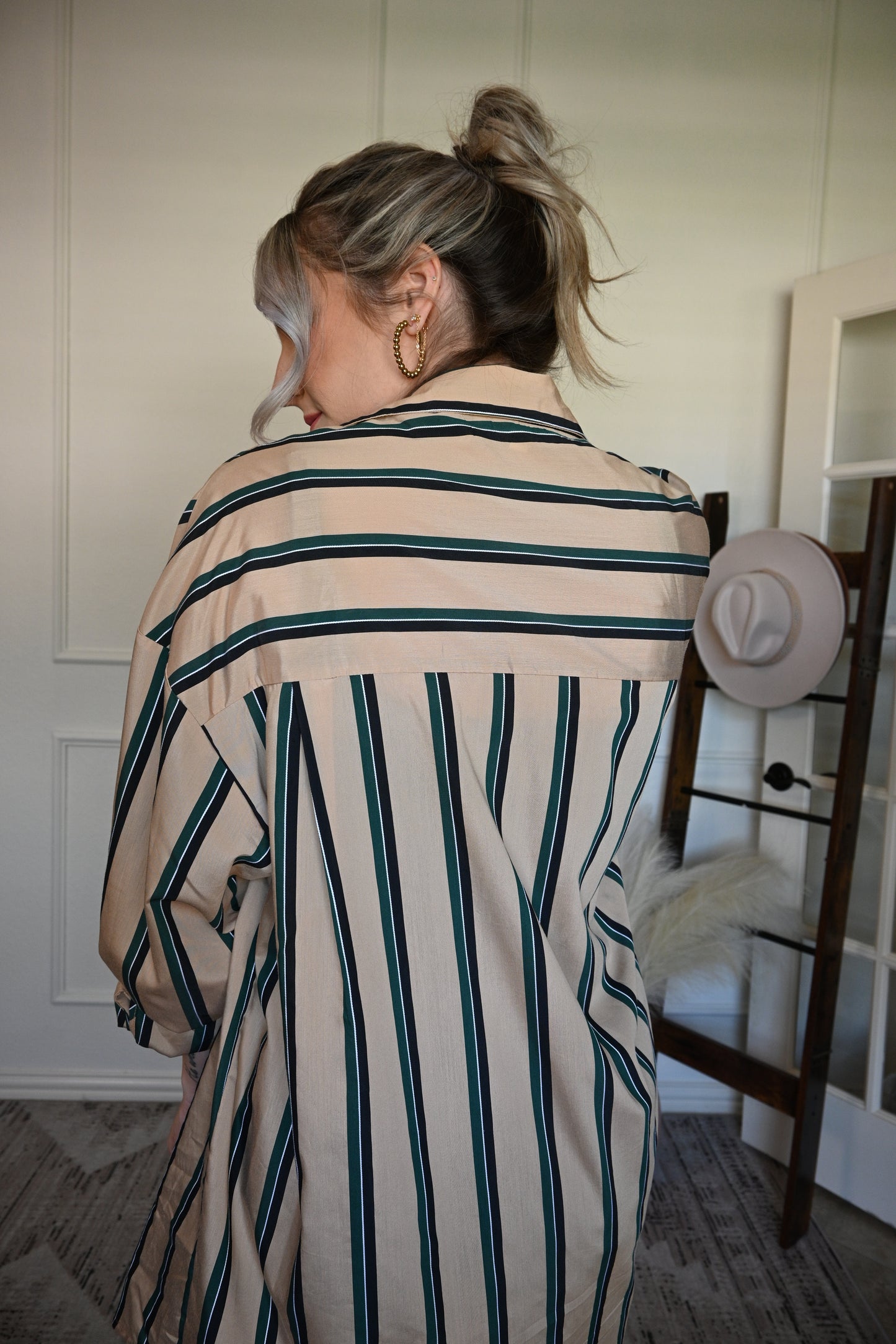 Person wearing a striped shirt/ dress standing in a room with a white wall and wooden floor.