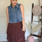 Woman in a denim vest over with a brown lace skirt.