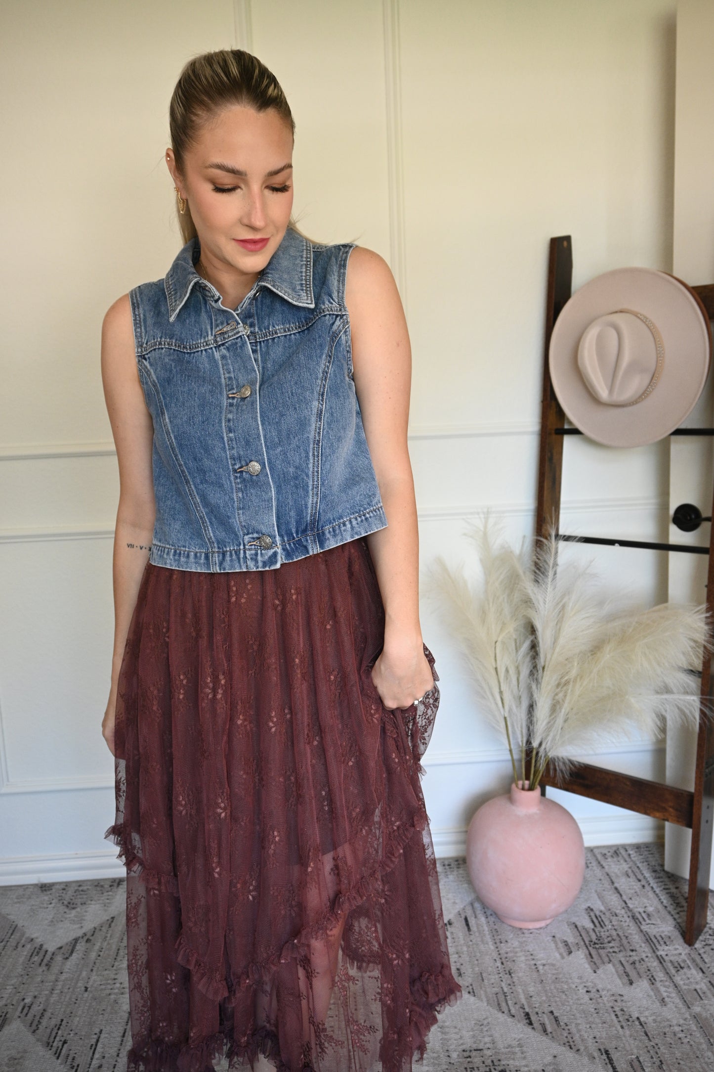 Woman in a denim vest over with a brown lace skirt.