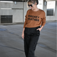 Model is wearing the brown crewneck sweater with the words "Whiskey Weather" in black on the front. It is paired with black satin pants and black heeled boots.