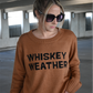 Up close image of the brown crewneck sweater with the words "Whiskey Weather" in black on the front. 