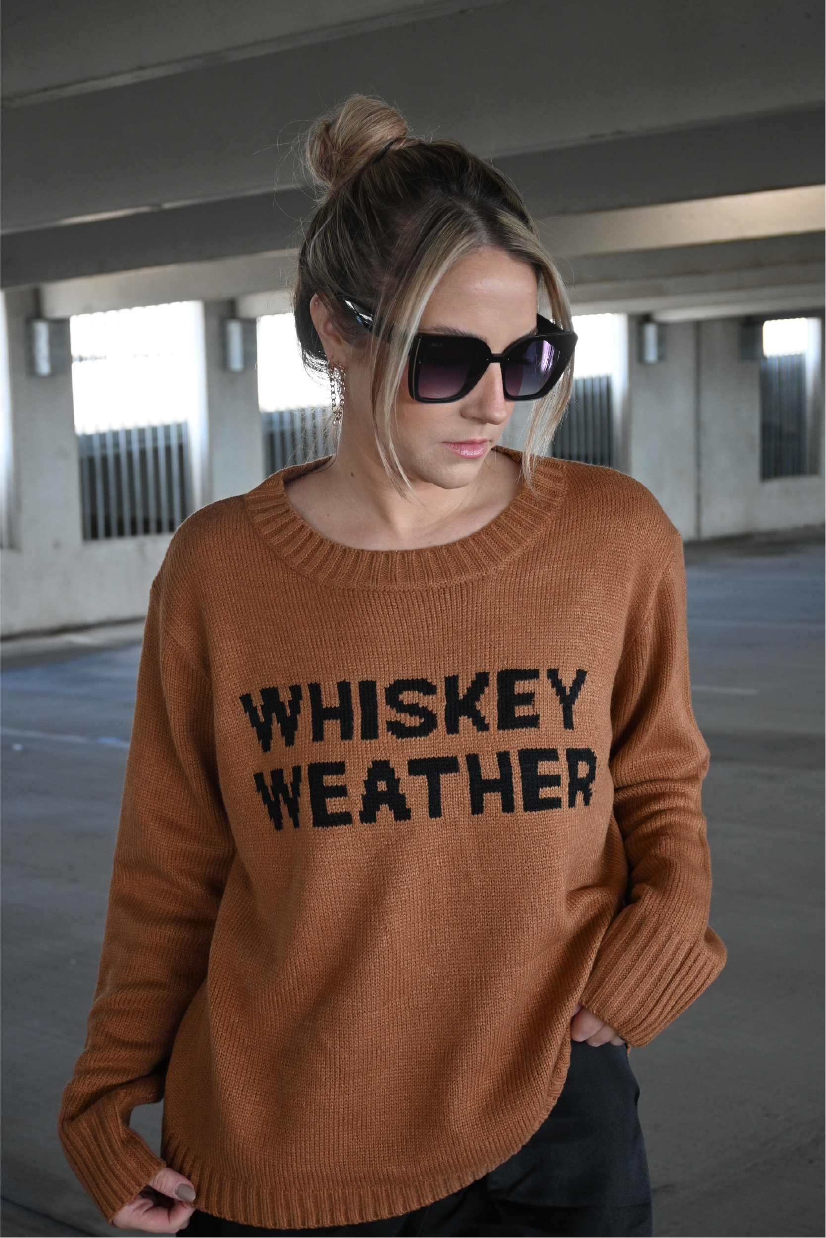 Up close image of the brown crewneck sweater with the words "Whiskey Weather" in black on the front. 