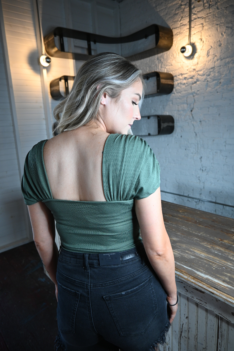 Back view of a woman wearing a hunter green bodysuit.