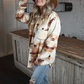 Woman looking away from the camera wearing a southwest style oversized jacket paired with skinny high rise light wash jeans and a tan fedora hat.