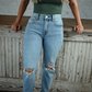 Woman wearing high rise light wash skinny jeans and a green tight fit shirt leaning on a distressed wood bar.
