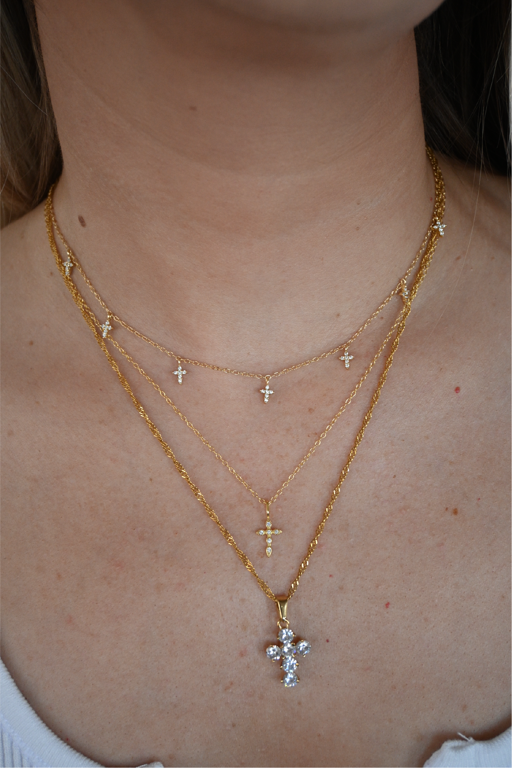 A close up shot of the seven cross necklace paired with the diamond cross necklace and vintage cross necklace around a woman's neck.