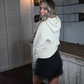 A back view of a woman looking back at the camera wearing a cream colored cropped hoodie and black frayed denim jean shorts.