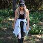 A woman standing looking down wearing a black corduroy mama hat with a black ribbed cropped cami and dark grey distressed skinny jeans with a distressed denim jacket around her waist. 