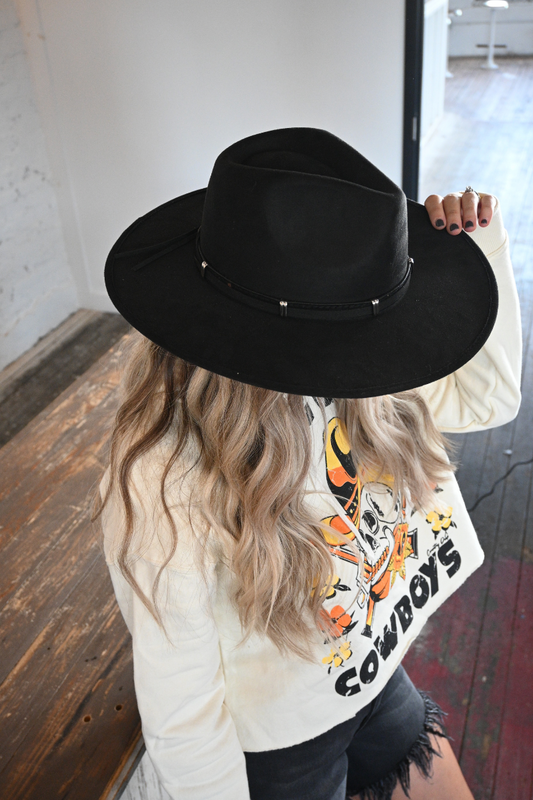 A top view of a woman wearing a black strap fedora hat with a white country style sweatshirt that says COWBOYS.