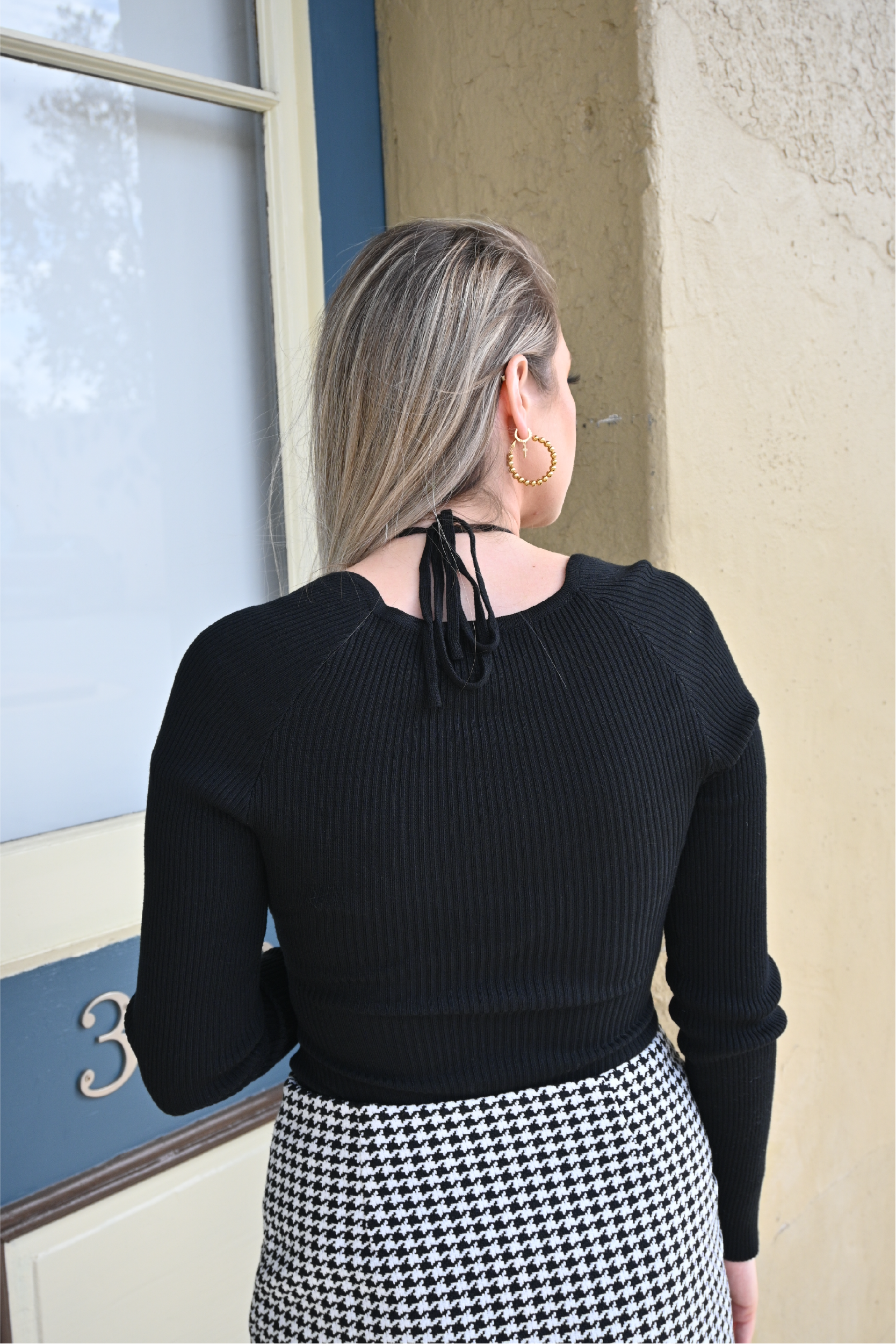 Model is showing the back of the black sweater bodysuit paired with the houndstooth mini skirt. 