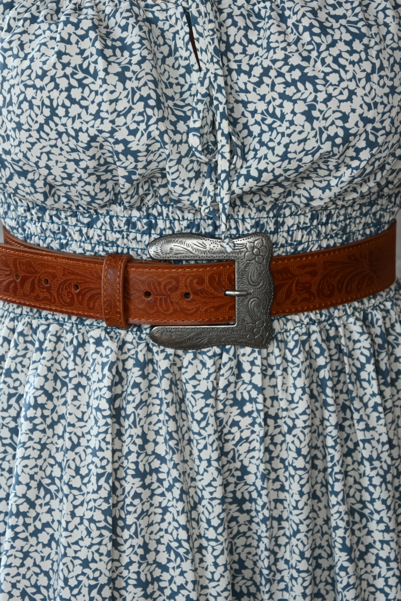 A photo of a tan, silver buckle belt with floral print design paired with a blue and ivory floral midi dress.