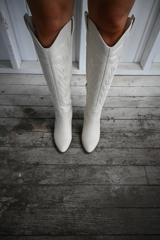 Womans legs wearing ivory colored western knee high boots.