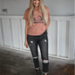 A woman is standing looking down smiling with one hand in her back pocket and the other hand by her side. She is wearing a rust colored mountains tee tucked into dark grey distressed skinny jeans cuffed at the bottom paired with faded black buckle ankle booties.